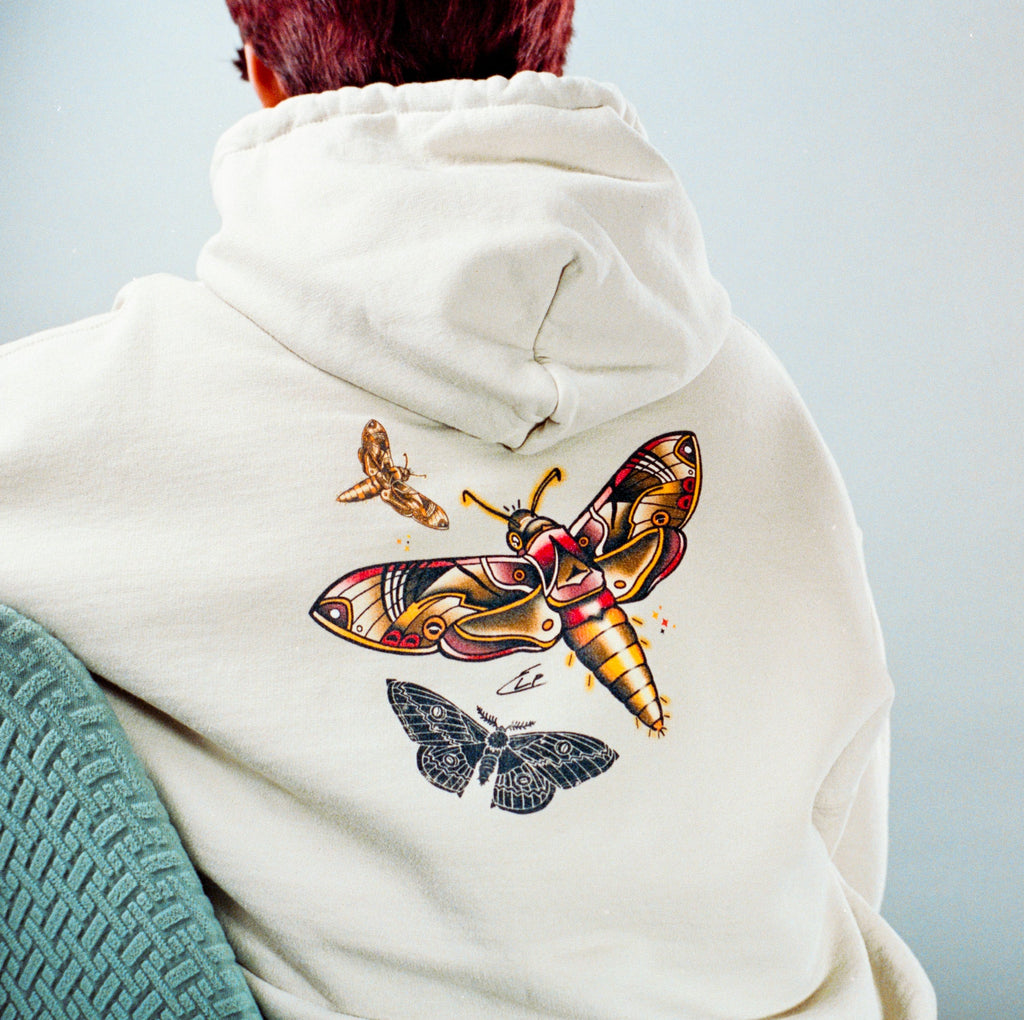 Person wearing a hoodie with moth designs on the back against a light gray background