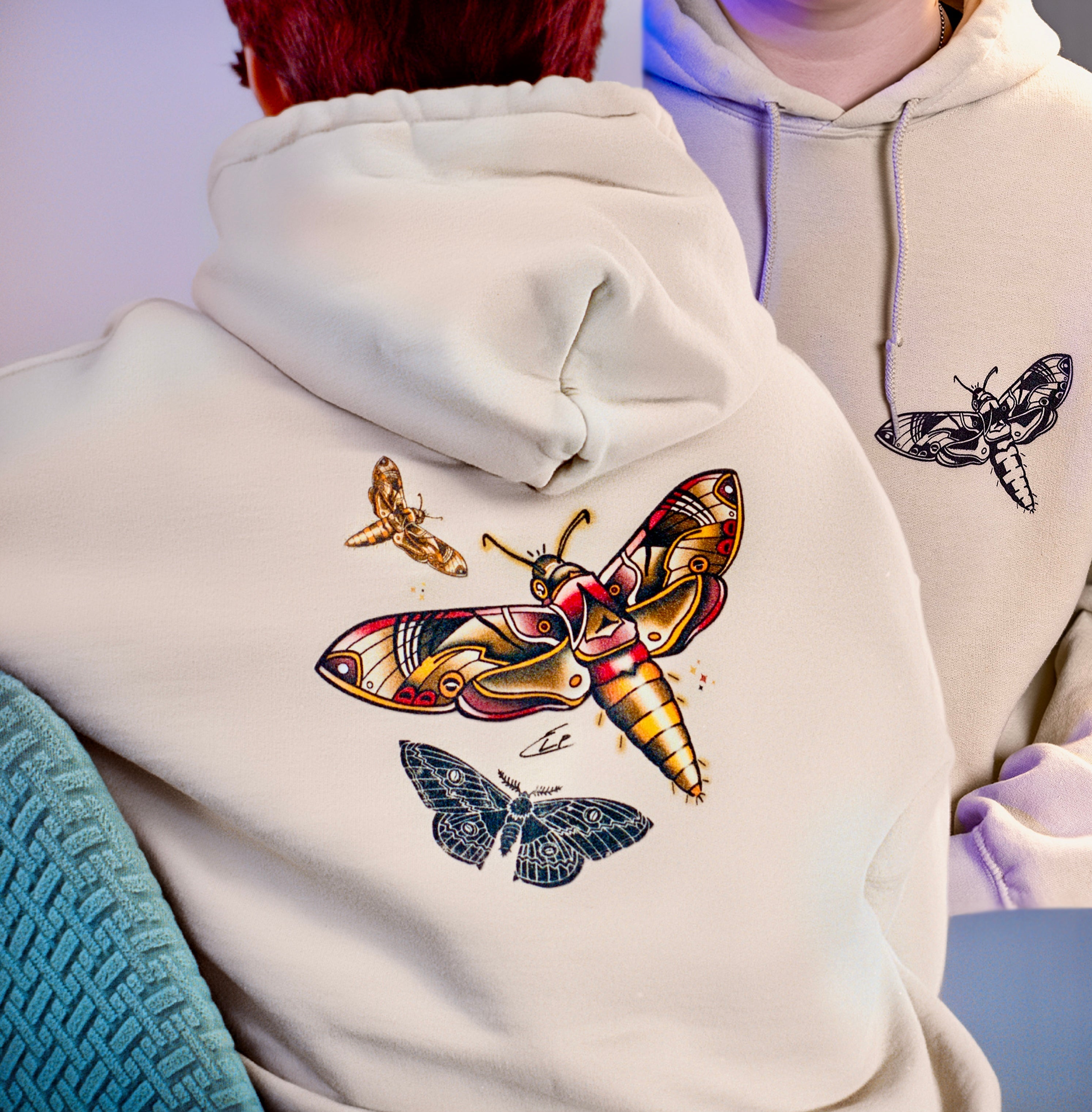 Light-colored hoodie with moth designs on a plain background