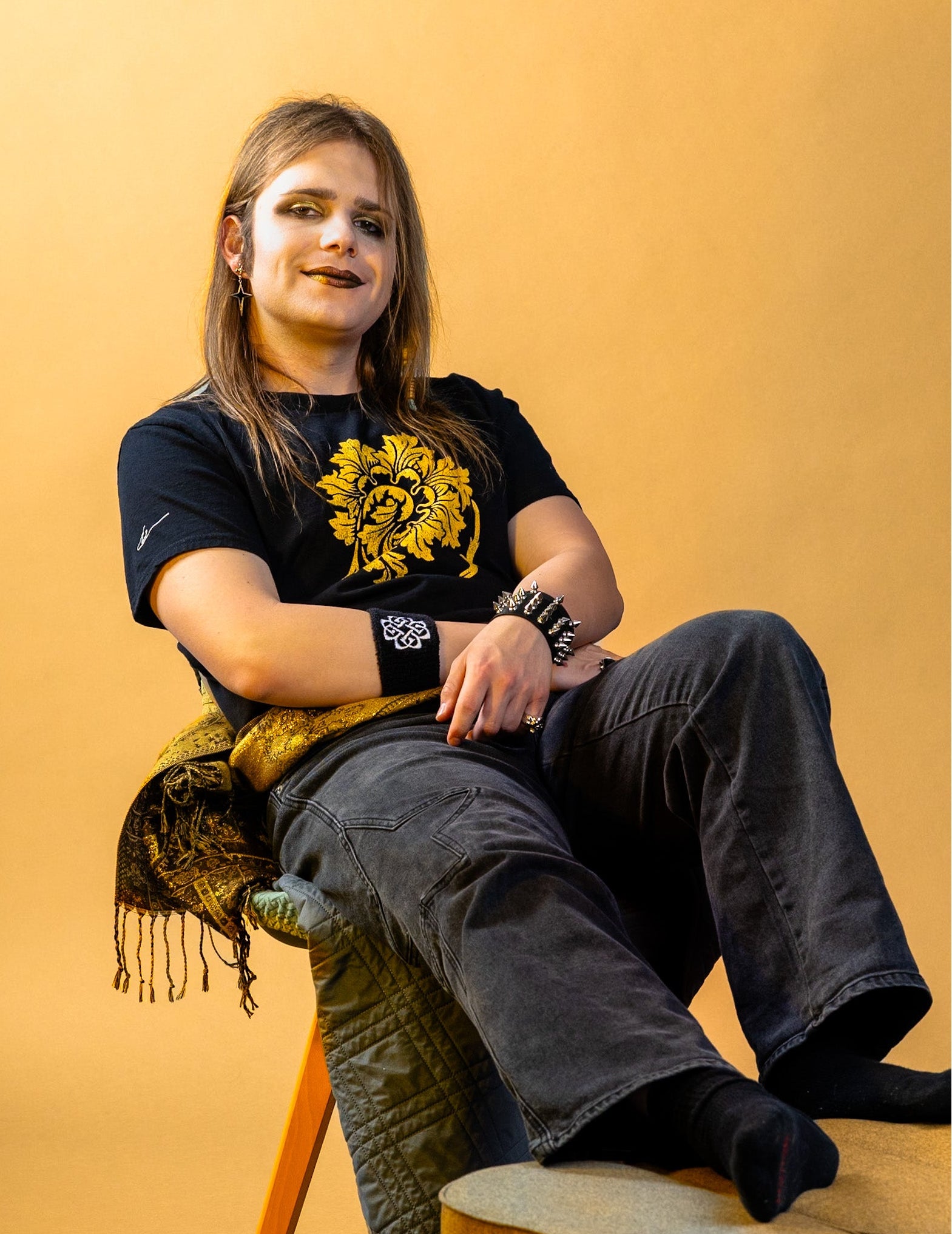 Person sitting on a stool against a yellow background wearing a black t-shirt with a yellow floral design.